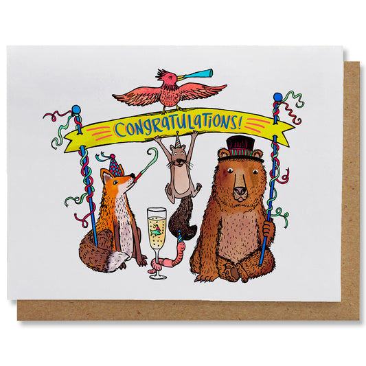 Illustrated greeting card featuring a fox and bear in fancy hats holding a yellow banner that reads “congratulations”. A party-hat-wearing squirrel hangs from the banner. A red bird blowing a noise-maker holds up the top of the banner. In between the fox and the bear is a champagne flute with a party-hat-wearing tiny fish swimming and a festive worm wrapped around the glass stem.
