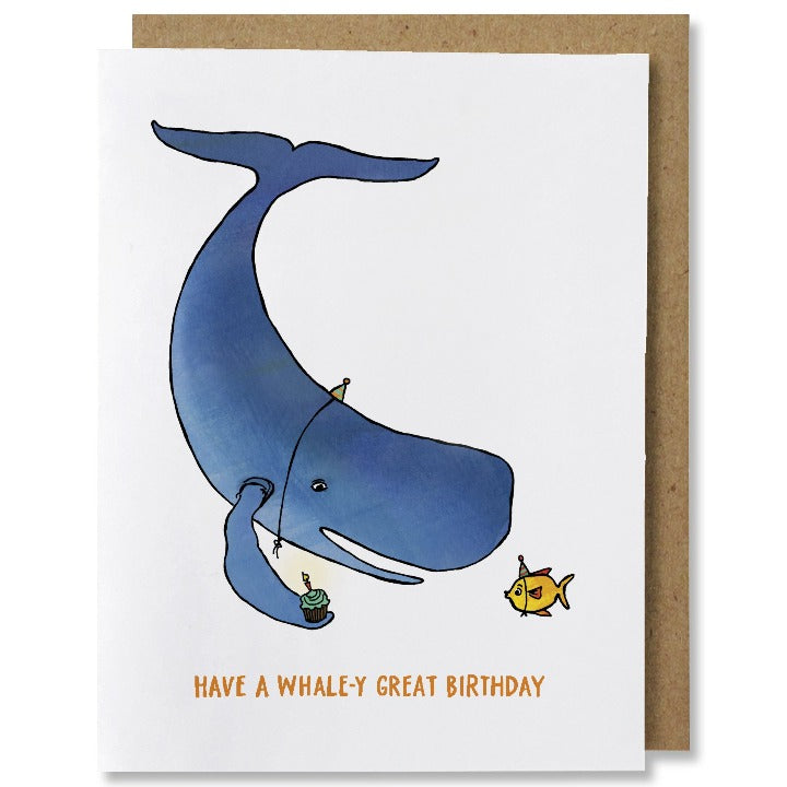 Illustrated birthday card featuring a blue whale on the left offering a cupcake with candle to a tiny yellow fish on the right, both wearing tiny party hats. Orange colored caption at bottom reads "have a whale-y great birthday"